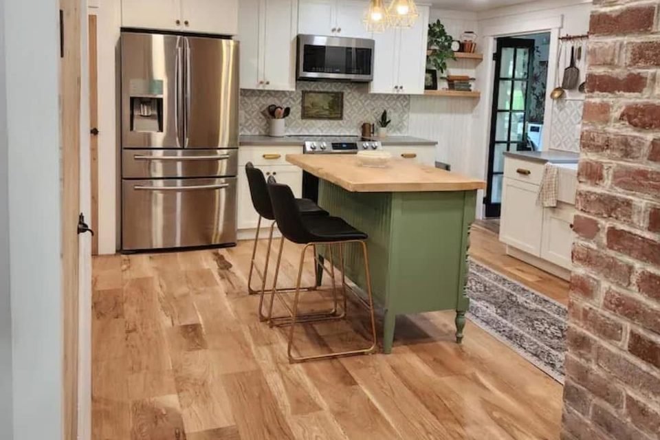 Bright kitchen with a green island, stainless refrigerator and wood floors